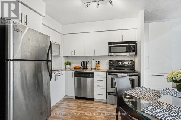 Kitchen with white cabinets, stainless steel appliances, granite countertops, and a dining table. - 207 - 80 Western Battery Road, Toronto