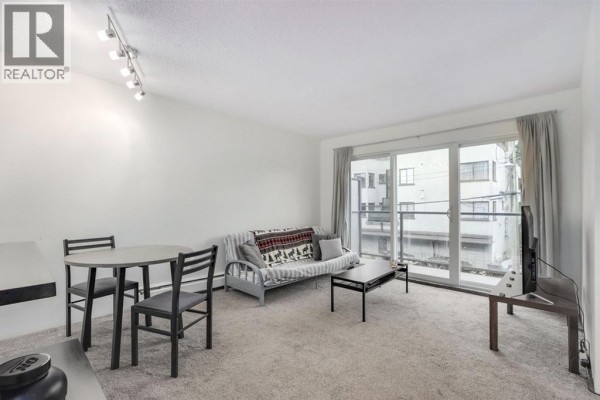 Living room with grey carpet, sofa, coffee table, and dining set by a sliding glass door. - 207 1450 Laburnum Street, Vancouver