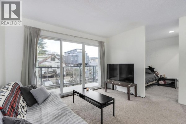 Living room with sofa, coffee table, and view of a bedroom separated by a partition. - 207 1450 Laburnum Street, Vancouver