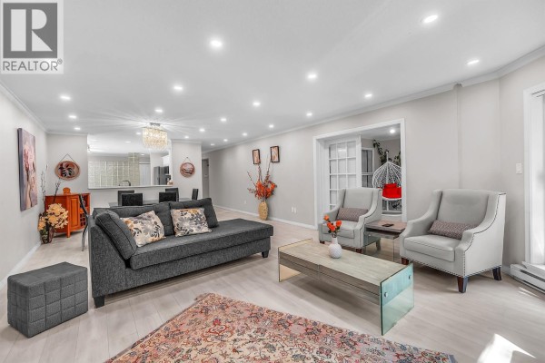 Living room with light wood floors, dark grey sectional, large TV, and dining area beyond. - 207 1500 Ostler Court, North Vancouver