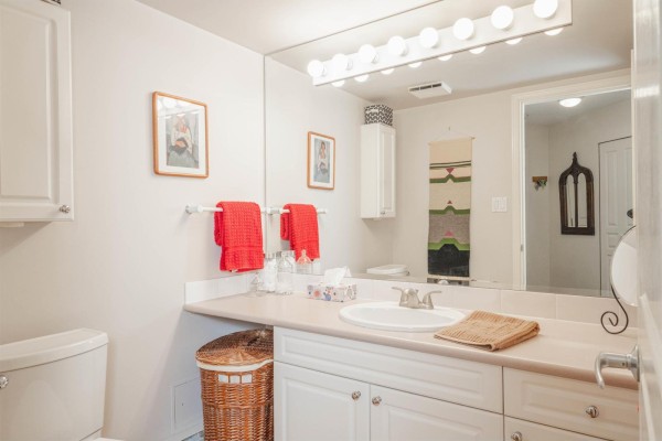 Bathroom vanity with double sinks, large mirror, and red towels on display. - 207 15466 North Bluff Road, White Rock