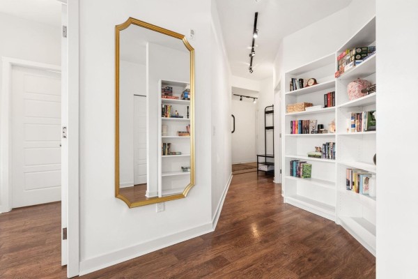 Interior hallway with white walls, dark wood floor, a gold ornate mirror, and built-in white bookshelves. - 203 23255 Billy Brown Road, Langley