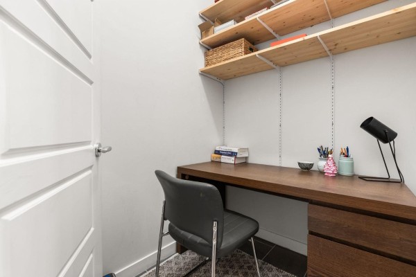 Small workspace with a dark wood desk, grey chair, white door, and natural wood shelves above. - 203 23255 Billy Brown Road, Langley