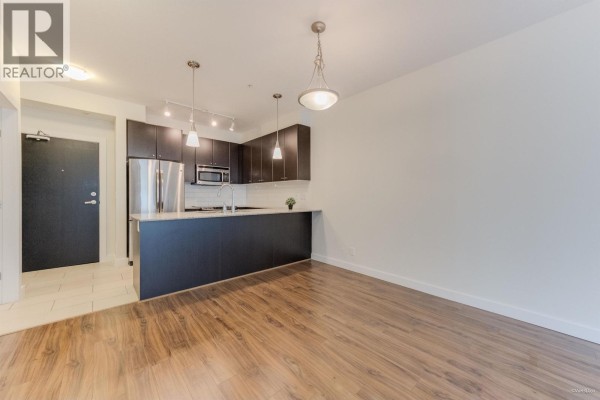 Open kitchen layout with dark cabinetry, light countertops, and pendant lighting - 207 240 Francis Way, New Westminster