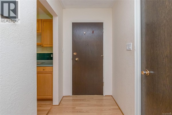 Apartment hallway looking towards the main door with a wood grain finish and beige walls. - 207 380 Brae Rd, Duncan