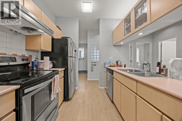 Galley kitchen with light wood cabinets, stainless steel appliances, and pink countertops. - 207 4951 Sanders Street, Burnaby