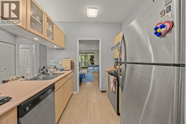 Kitchen with light wood cabinets, stainless steel appliances, and view into living room. - 207 4951 Sanders Street, Burnaby