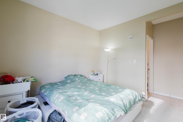 Bedroom with a double bed, bedside table, and soft lighting against a neutral wall. - #207 9910 111 St Nw, Edmonton