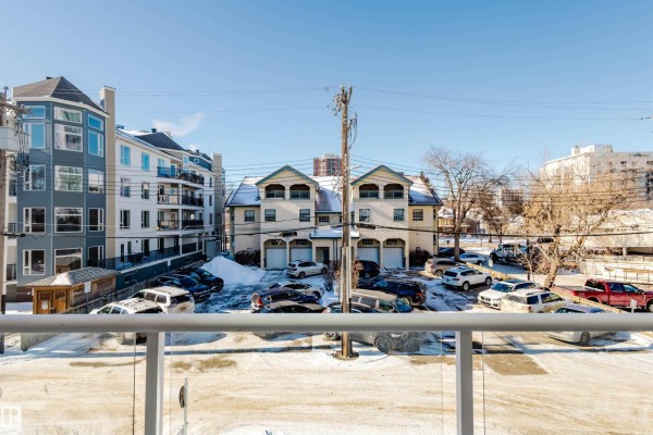 View from the balcony showing parked cars, nearby buildings, and clear blue sky. - #207 9910 111 St Nw, Edmonton