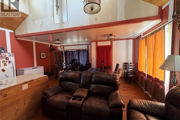 Living room with brown leather sofa, orange curtains, and a wooden dining table with chairs. - 207 Main Street, Hudson Bay