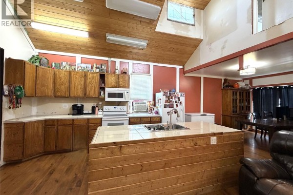 Kitchen with wooden cabinets, white appliances, a double sink island, and a vaulted wood ceiling. - 207 Main Street, Hudson Bay