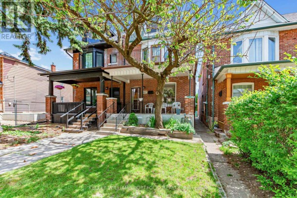 Front view of a brick semi-detached house with a manicured lawn and trees. - 207 Symington Avenue, Toronto