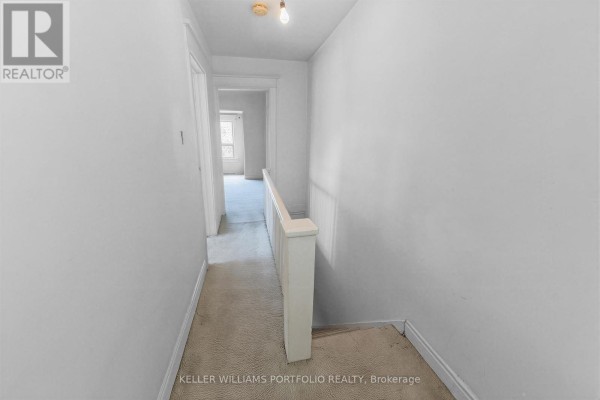 Hallway on the upper floor with light grey walls, beige carpet, and white railing. - 207 Symington Avenue, Toronto