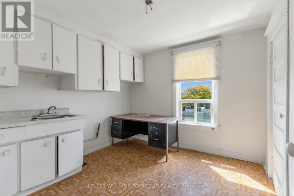 Room with white cabinets, a sink, a desk, and a large window overlooking trees. - 207 Symington Avenue, Toronto