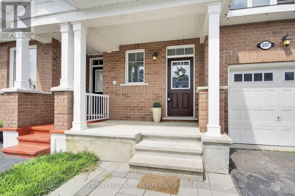 Close-up of a townhouse front entrance with a brick facade, covered porch, and white columns. - 207 Willow Aster Circle, Ottawa