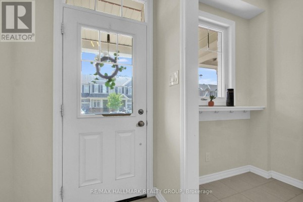View through a glass-paneled front door showing a simple entryway with beige walls and a window. - 207 Willow Aster Circle, Ottawa