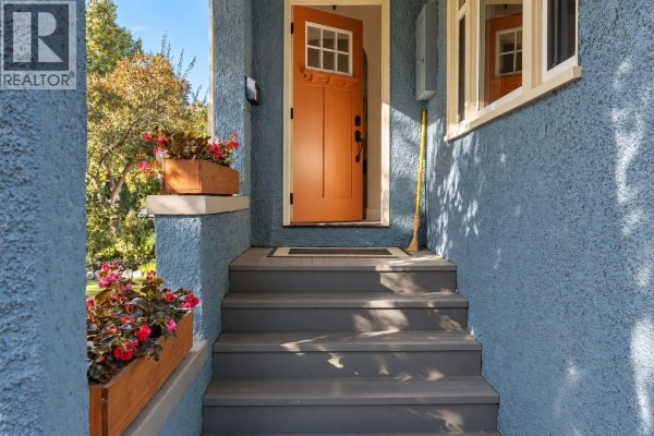 Close-up of the light blue house entrance with gray steps, orange door, and flower planters. - 2071 Abbott Street, Kelowna