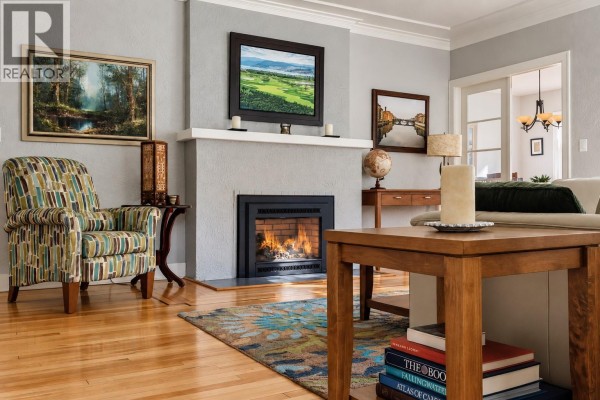 Living room with a fireplace, armchair, coffee table, and artwork on a light gray wall. - 2071 Abbott Street, Kelowna