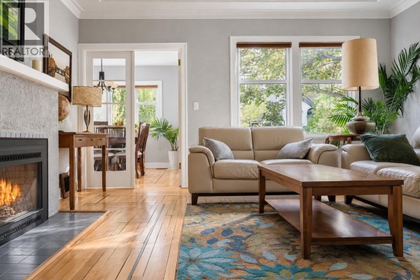 Living room with a fireplace, beige sofas, coffee table, and view into a dining room. - 2071 Abbott Street, Kelowna