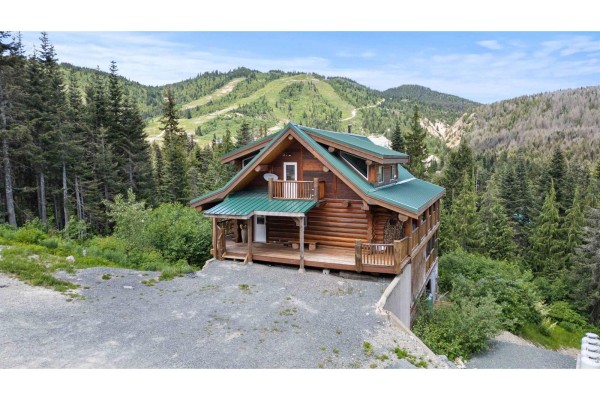 Log cabin nestled in a snowy mountain landscape with a ski slope visible in the distance. - 20758 Edelweiss Drive, Mission