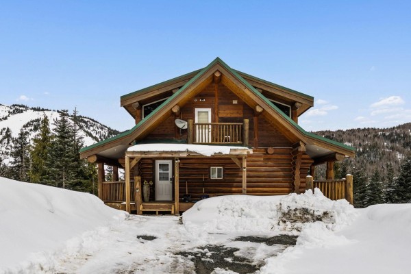 Side view of the log cabin showing its two stories, wooden exterior, and snowy surroundings. - 20758 Edelweiss Drive, Mission