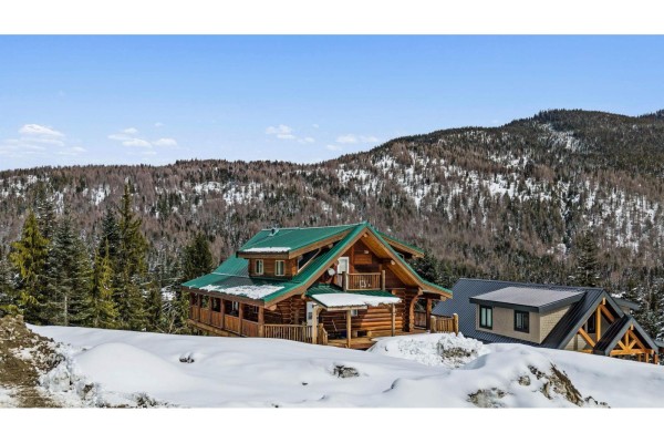 Front view of the wooden log cabin with a covered porch, white door, and snow-filled driveway. - 20758 Edelweiss Drive, Mission