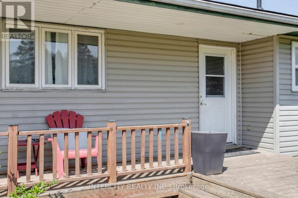 A red Adirondack chair sits on a wooden deck next to a white door and a large grey planter. - 2076 15th Side Road, New Tecumseth
