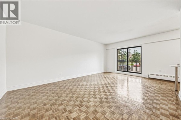 Living room with parquet flooring, white walls, and a large window with balcony access. - 2077 Prospect Street Unit# 104, Burlington