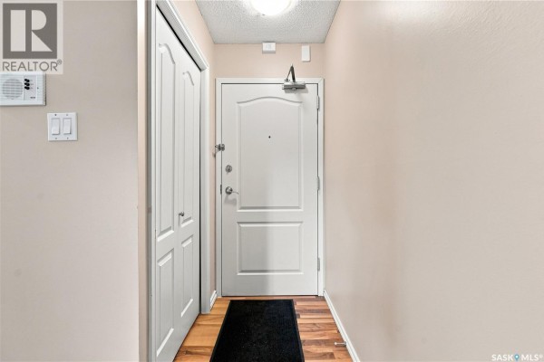 Apartment entryway with a white door, double closet, and beige walls. - 207e 1121 Mckercher Drive, Saskatoon