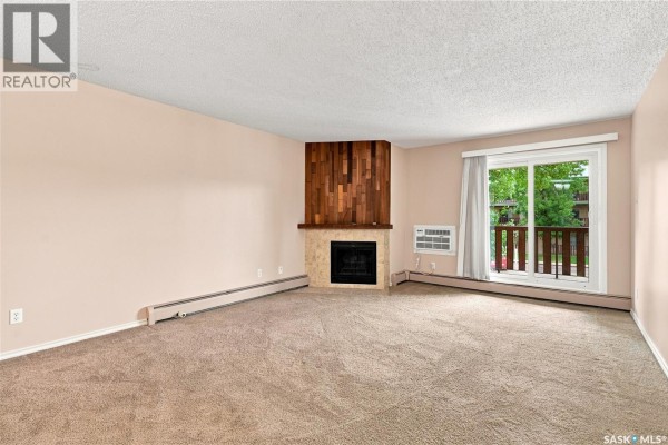 Living room with beige carpet, fireplace with wood accent, and sliding glass door. - 207e 1121 Mckercher Drive, Saskatoon