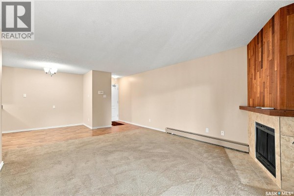 Living room with beige carpet, fireplace, and view of entryway from living space. - 207e 1121 Mckercher Drive, Saskatoon