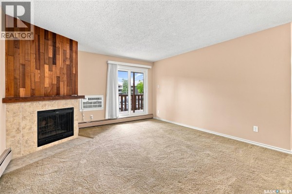 Living room with beige carpet, fireplace, and view of balcony through sliding door. - 207e 1121 Mckercher Drive, Saskatoon