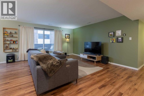 Living room with sectional sofa, television, and window view of building exterior. - 208, 2207 8 Avenue S, Lethbridge