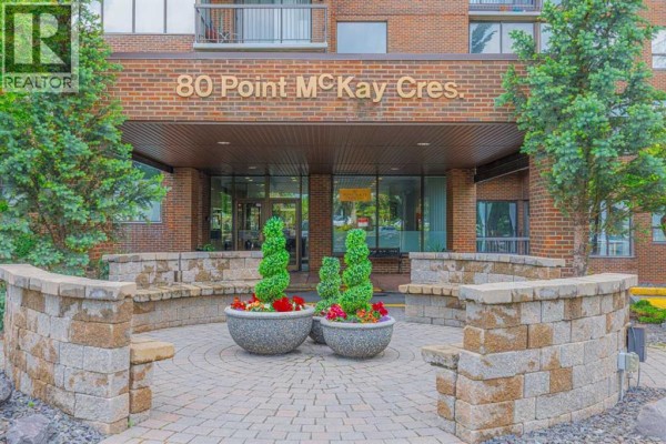 Building entrance with a sign reading "80 Point McKay Cres." and stone seating. - 208, 80 Point Mckay Crescent Nw, Calgary