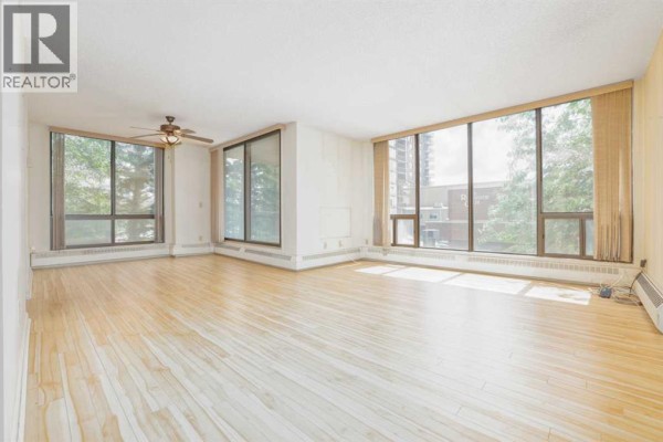 Spacious apartment living room with light wood floors and large windows on multiple walls. - 208, 80 Point Mckay Crescent Nw, Calgary
