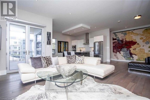 Living room and kitchen area with white sectional sofa, glass coffee table, and island. - 208 - 1705 Fiddlehead Place, London North
