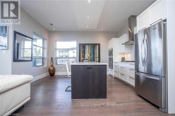 Kitchen island with dark wood cabinets and stainless steel appliances in open-concept living space. - 208 - 1705 Fiddlehead Place, London North