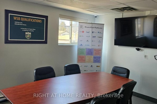 Conference room with wood table, chairs, large TV screen, and company banner. - 208 - 200 Bond Street W, Oshawa