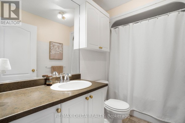 Bathroom vanity with a white sink, brown countertop, and a large mirror above the toilet and tub. - 208 - 2927 Laurier Street, Clarence Rockland