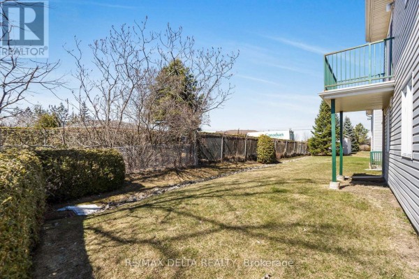 Backyard with a grassy lawn, green hedges, a chain-link fence, and a balcony with green railings. - 208 - 2927 Laurier Street, Clarence Rockland