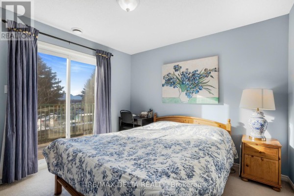 Bedroom with light blue walls, a sliding glass door to a balcony, a wooden bed, and a desk. - 208 - 2927 Laurier Street, Clarence Rockland