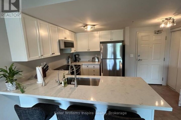 Apartment kitchen with white cabinets, stainless steel appliances, and quartz island. - 208 - 625 St David Street S, Centre Wellington