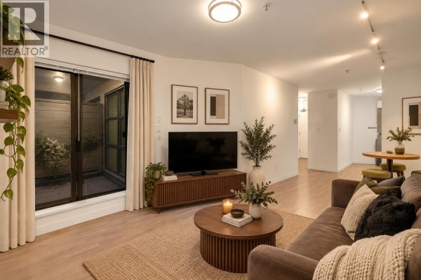 Living room with a large television, sliding glass doors, and light wood floors extending into a hallway. - 208 1106 Pacific Street, Vancouver