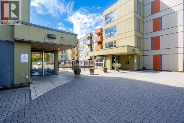 Entrance to apartment building 12075 with glass doors and surrounding pavement. - 208 12075 228 Street, Maple Ridge