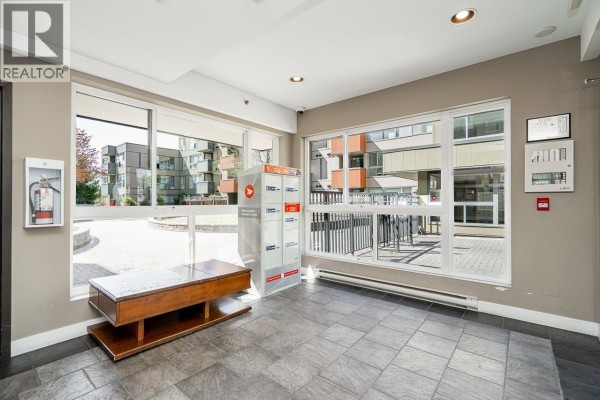 Building lobby with mailboxes, a wooden bench, and large windows overlooking the courtyard. - 208 12075 228 Street, Maple Ridge