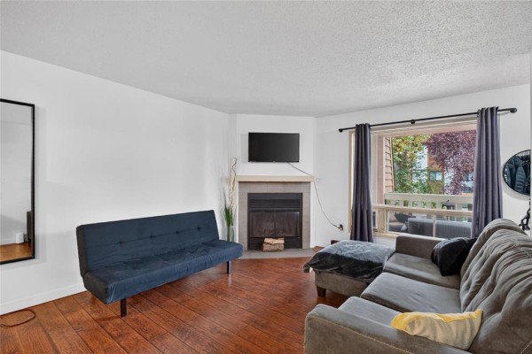 Living room featuring a grey sectional sofa, fireplace with tile surround, and a window overlooking trees. - 208 1760 Henderson Highway, Winnipeg