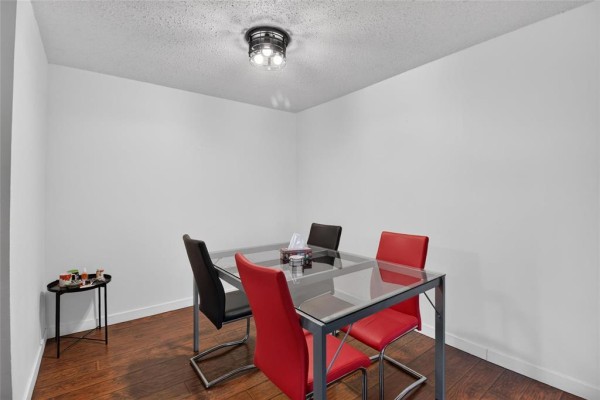 Dining area with a glass-top table, red and black chairs, and hardwood floors. - 208 1760 Henderson Highway, Winnipeg