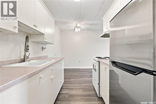 Apartment kitchen with white cabinets, stainless steel refrigerator, and sink. - 208 2830 Gordon Road, Regina