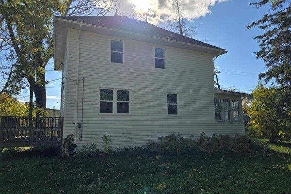 Side view of a white house with multiple windows and vinyl siding, surrounded by green grass. - 208 2nd Street, Oakville