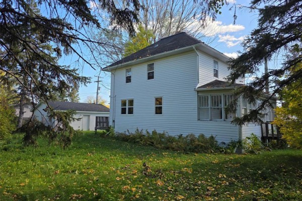Side and back view of a white house with a detached two-car garage, surrounded by grass and trees. - 208 2nd Street, Oakville